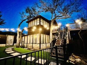 A two-story house with a stone facade, a wooden deck, and a staircase leading to a second level. - Little Big Sunset In Private Oasis (Volente)