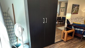 Un salon moderne avec une armoire en bois foncé, un canapé à motifs, une petite table basse en bois et un ventilateur sur pied.