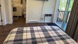 Une chambre dotée d’un grand lit, d’un téléviseur fixé au mur, d’une porte-fenêtre coulissante donnant sur un balcon et d’une salle de bain visible à travers une porte ouverte.