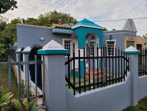 Stroll through the gated entrance, flanked by columns, to a covered porch area surrounded by lush greenery.