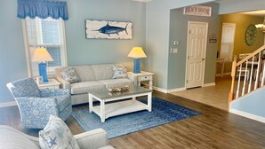A living room with a sofa, armchair, coffee table, and lamps. There is a painting of a fish on the wall and a sign that reads 'BEACH HOUSE'. - 5-Star*Sunset Island Townhouse, close to POOLS, Beach Chairs, FREE Linens/Towels (Ocean City)