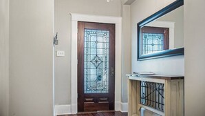 Un couloir avec une porte en bois ornée d’un vitrail, un lustre et un miroir placé au-dessus d’une console en bois.