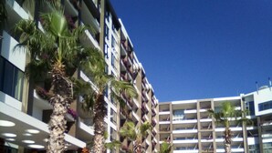 A modern hotel with multiple floors, outdoor pool area, and palm trees.