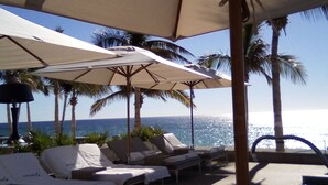A beachside lounge area with sun loungers and umbrellas, overlooking the ocean.
