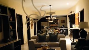 Ein modernes Wohnzimmer mit Sofa, Couchtisch und Dekoration. Im Hintergrund ist eine Essecke mit einer Kronleuchter zu sehen.