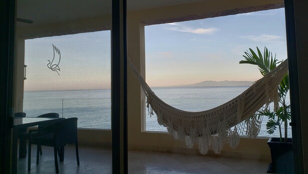 Ein Zimmer mit Meerblick, einer Hängematte und einem Tisch mit Stühlen.