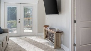 A living room with a sofa, a coffee table, a flat-screen TV mounted on the wall, and a sliding glass door leading to a balcony. - Old Dauphin Way Historic Home - Unit 6 (Mobile)