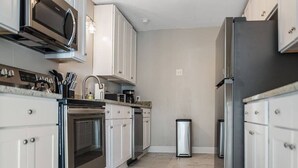 A modern kitchen with white cabinets, stainless steel appliances, and a tiled floor. - Old Dauphin Way Historic Home - Unit 6 (Mobile)