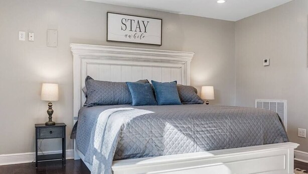 A bedroom with a bed, two bedside tables, a wall-mounted sign, and a radiator. - Old Dauphin Way Historic Home - Unit 6 (Mobile)
