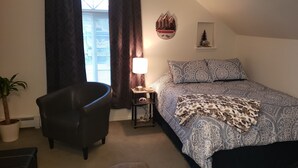 A bedroom with a bed, a chair, a bedside table with a lamp, a wall decoration, and a potted plant. - Studio Close to Everything (Belgrade)