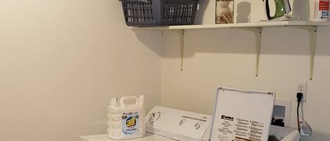 A laundry room with a washing machine, a dryer, a basket, and cleaning supplies.