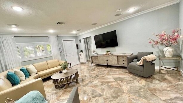 Ein geräumiges Wohnzimmer mit einem beigefarbenen Sofa, einem grauen Sessel, einem Couchtisch und einem flachbildfernseher, der an der Wand montiert ist.