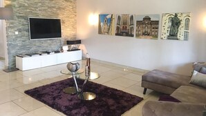 A modern living room with a stone wall, a flat-screen TV, a glass coffee table, a sofa, and artwork on the wall. - Stunning 3-Bed House in Tema-Ahenfie Villa (Tema Spintex)