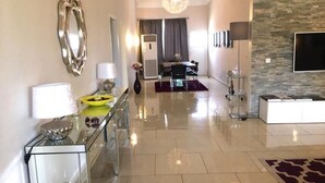 A modern living room with a glass coffee table, a dining area with a table and chairs, a TV mounted on the wall, and a stone accent wall. - Stunning 3-Bed House in Tema-Ahenfie Villa (Tema Spintex)