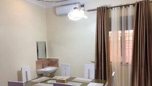 Un comedor con mesa de vidrio, sillas blancas, un lavamanos blanco y un espejo en la pared.