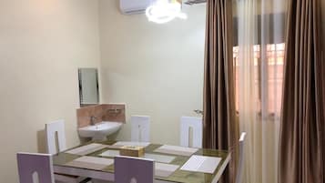 A dining area with a glass table, white chairs, a white sink, and a mirror on the wall.