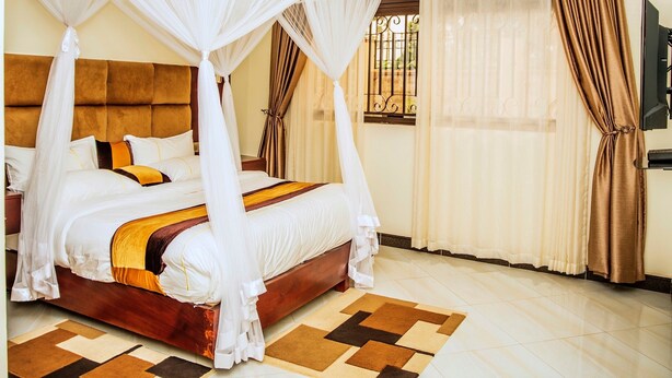 Una cama con dosel y cuatro columnas, con cabecera de madera, alfombra estampada y cortinas en las ventanas.