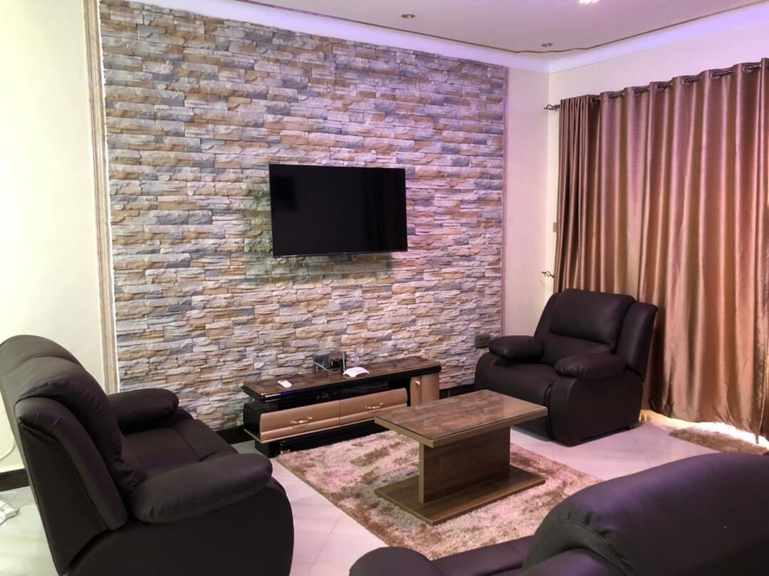 Ein modernes Wohnzimmer mit Steinwand, Flachbildfernseher, Ledersofas und einem Couchtisch.