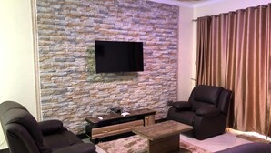 Una sala de estar moderna con una pared de piedra, un televisor de pantalla plana, sofás de cuero y una mesa de centro.