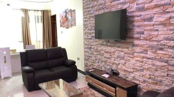 Ein Wohnzimmer mit Steinsandsteinwand, einem Flachbildfernseher, einem Ledersofa und einem Glastisch.