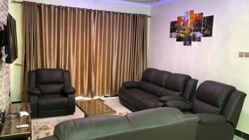 Una sala de estar con un sofá de cuero marrón, un sillón de cuero negro y una mesa de centro de vidrio.