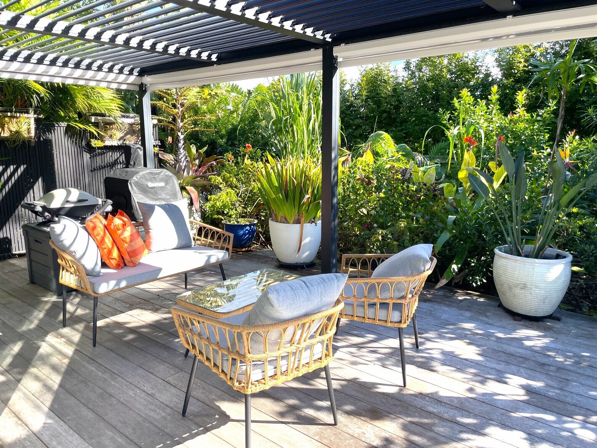 Un patio al aire libre con mobiliario de mimbre, una parrilla y plantas en macetas.