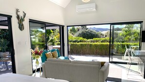 A modern bedroom with a large bed, a sofa, and a balcony with a view of greenery. - Gorgeous private studio apartment midway between Omaha & Matakana (Point Wells)