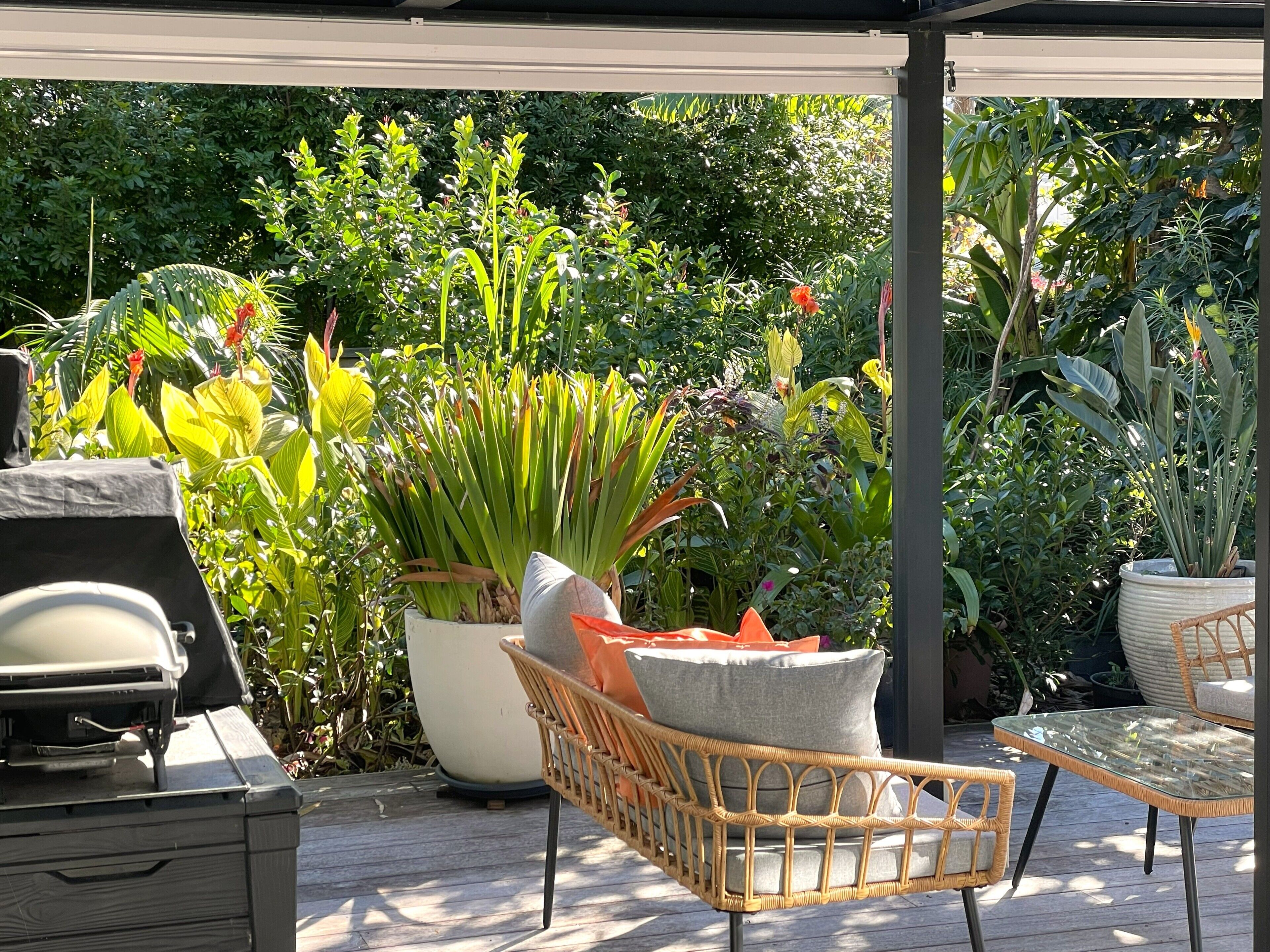 A covered outdoor seating area with wicker furniture, a grill, and various potted plants.