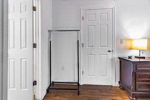 A hallway with a white door, a white door frame, a white wall, a wooden floor, and a dark-colored cabinet with a lamp on top. - Stunning Pool Home, Near Siesta Key & Dog Friendly (Sarasota)