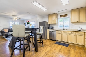 A modern kitchen with a central island, stainless steel appliances, and light wooden cabinets.