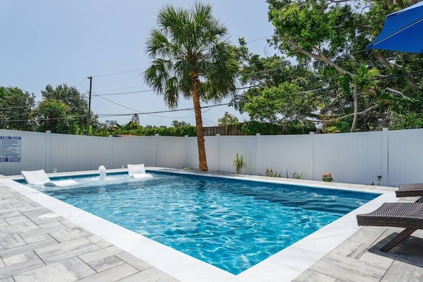 A rectangular swimming pool with clear blue water, surrounded by a white fence, and a palm tree in the center.