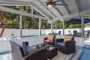 A covered outdoor area with wicker furniture, a glass table, and umbrellas. - Stunning Pool Home, Near Siesta Key & Dog Friendly (Sarasota)