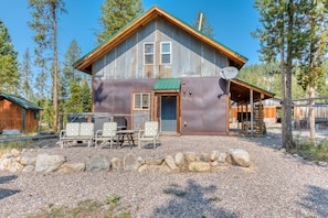A rustic cabin with a metal exterior, a covered porch, and a gravel driveway.