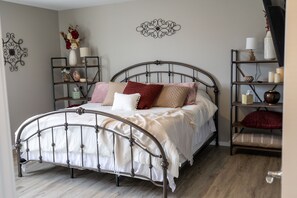 Un dormitorio ordenado con una cama de estructura metálica, un estante junto a la cama con objetos decorativos y un adorno fijado a la pared.