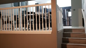 Una escalera con escalones de madera y barandillas blancas, que conduce a una cocina moderna con electrodomésticos de acero inoxidable y una encimera blanca.