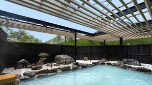 A hot spring area with a wooden bench, rocks, and a pergola structure.