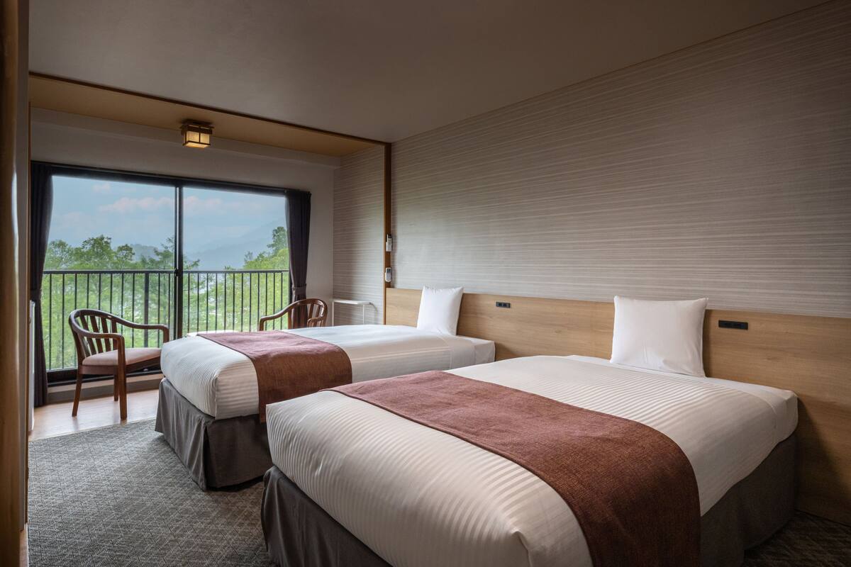 Habitación de hotel con dos camas, un balcón y vistas al exterior.