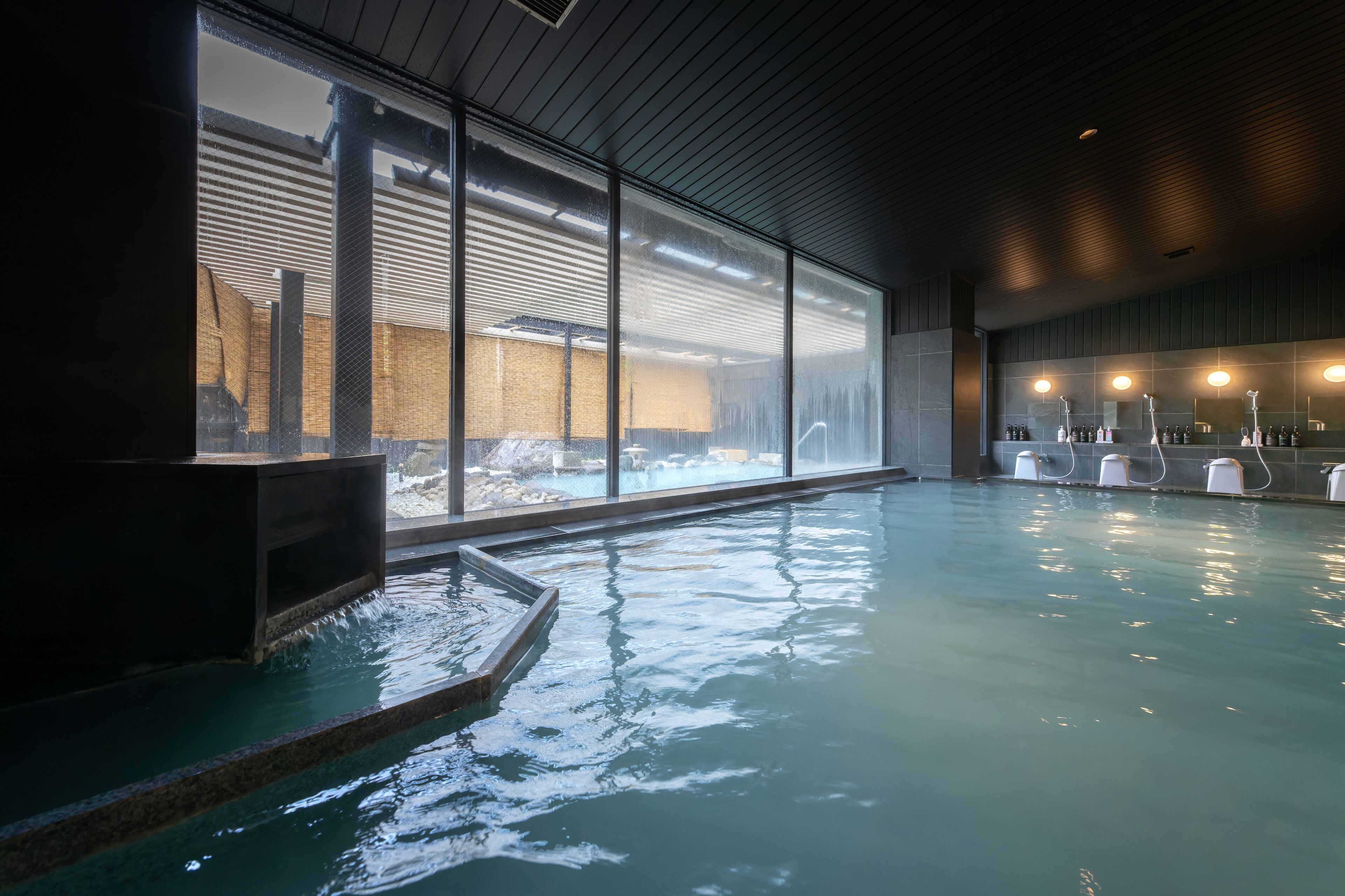 An indoor swimming pool with clear glass walls, a wooden ceiling, and a visible brick structure outside.