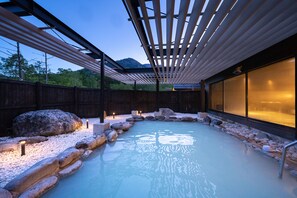 Un espace de baignade dans une source thermale, avec une terrasse en bois, des rochers et une vue sur les montagnes.