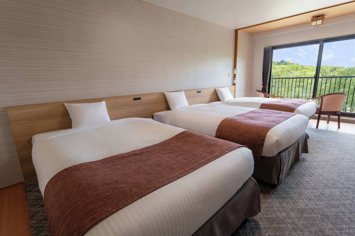 Habitación de hotel con tres camas, balcón y vistas, y diseño moderno.