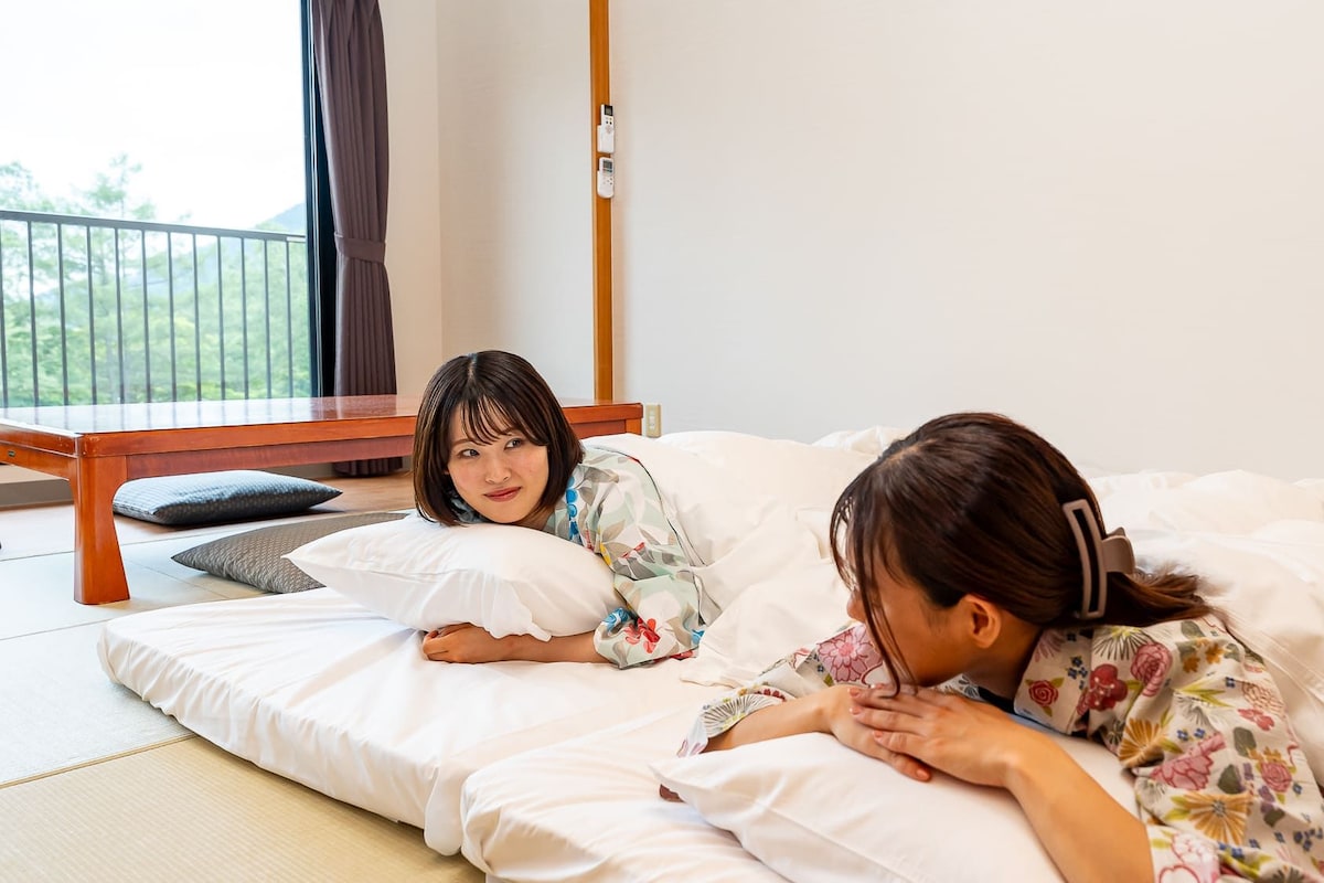 A room with tatami flooring, a low wooden table, and a view of greenery outside.