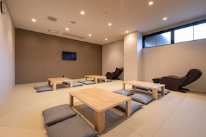 A room with tatami mats, wooden tables, and black massage chairs.
