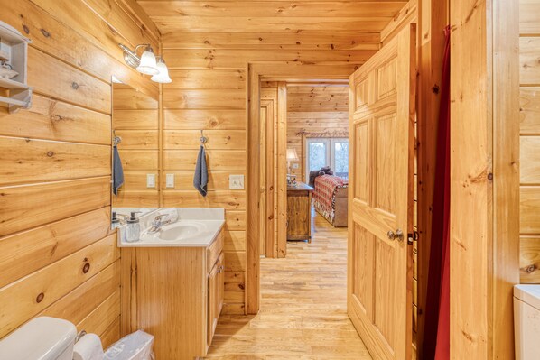 A wooden cabin interior with a wooden floor, a sink, a toilet, and a mirror.