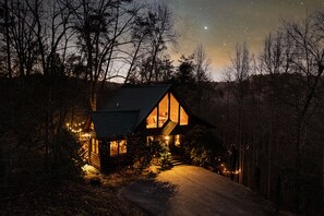 A cabin with a large window, a wooden exterior, and a pathway leading to the entrance.