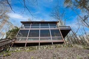 Una cabaña de madera de varios niveles con balcón, rodeada de árboles y un cielo despejado.
