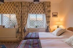 A bedroom with two beds, a radiator, a window with curtains, a lamp, and a framed picture on the wall.