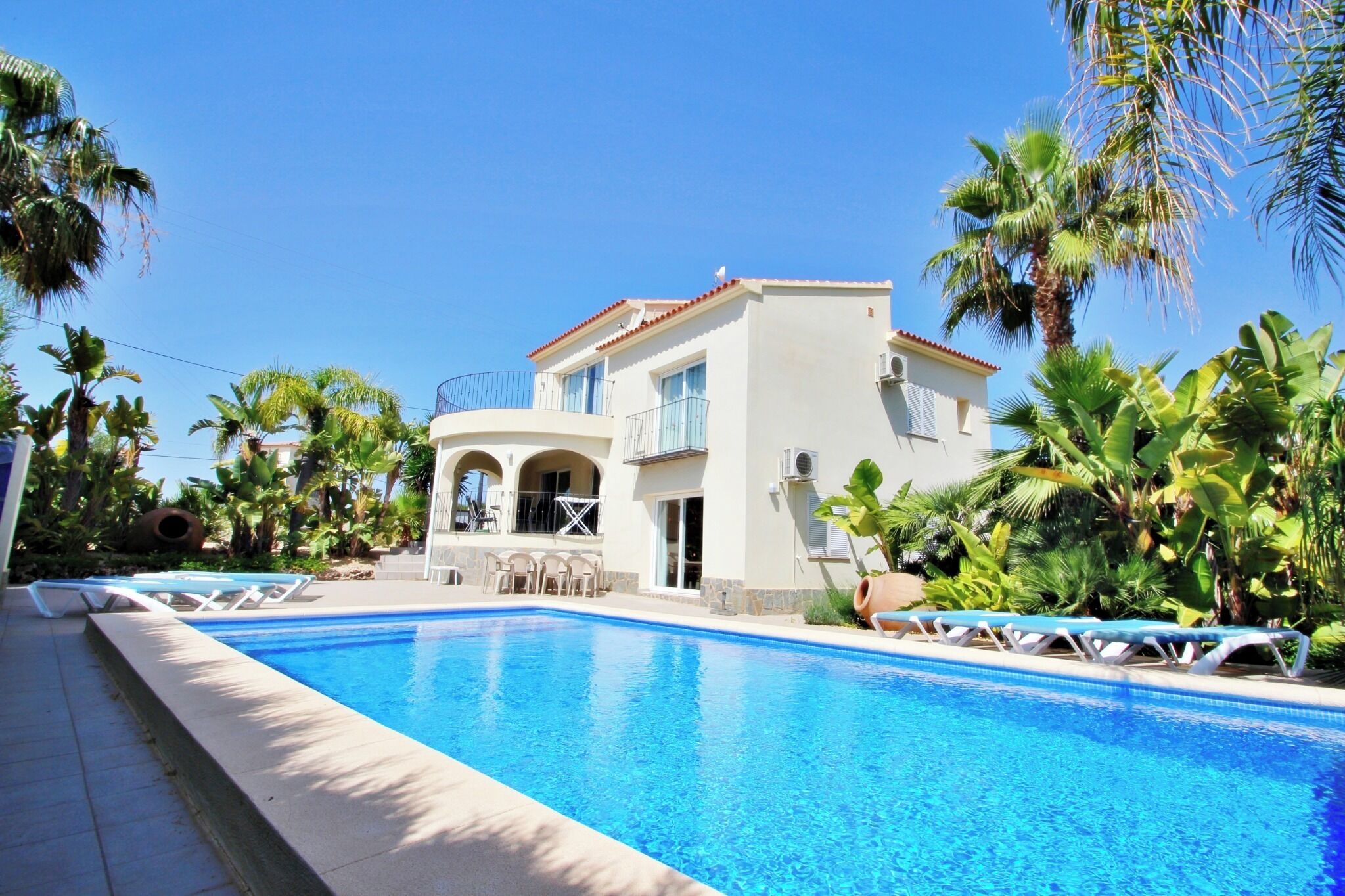 A two-story building with a swimming pool, surrounded by palm trees.