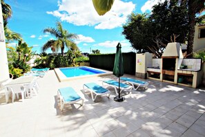 A pool area with lounge chairs and a small outdoor kitchen.