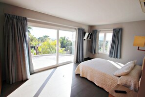 A bedroom with a bed, a TV, and a balcony with curtains.