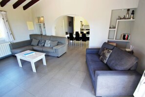 Amplia sala de estar con sofá gris, una mesa de centro blanca y un comedor con sillas y una mesa.